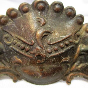 May include: A close-up of a decorative metal ornament with a peacock design. The ornament is made of a dark metal with a distressed finish. The peacock design is intricate and detailed, with a fan of feathers and a head with a crown.
