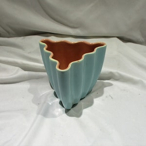 May include: A light blue ceramic planter with a scalloped edge and a peach-colored interior. The planter is shaped like a triangle.