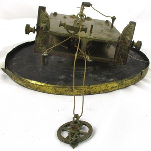 Peut inclure: M&eacute;canisme d'horloge antique en laiton et m&eacute;tal. Le m&eacute;canisme est mont&eacute; sur une base circulaire avec un bord dor&eacute;. Un pendule est suspendu &agrave; la face de l'horloge. Les composants de l'horloge montrent des signes d'&acirc;ge et d'usure.