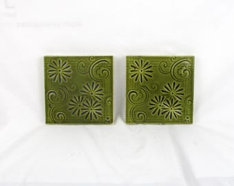 May include: Two green ceramic tiles with a floral design. The tiles have a raised pattern of stylized flowers and swirls.