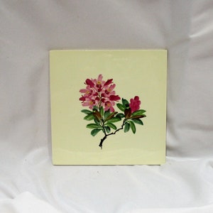 May include: A square tile with a hand-painted design of pink flowers and green leaves on a pale yellow background.