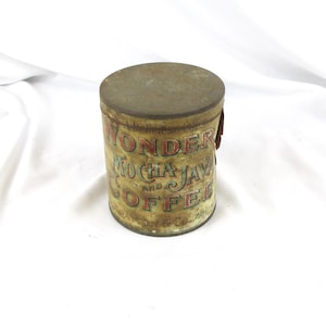 May include: A cylindrical vintage metal coffee tin with a weathered patina. The label features the text WONDER MOCHA AND JAVA COFFEE and BRAYTON & CO. BOSTON in red and green lettering against a tan background. The lid is a flat, circular metal disc.