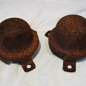 May include: Two rusty metal dome-shaped objects with three legs each. The objects are on a white surface.