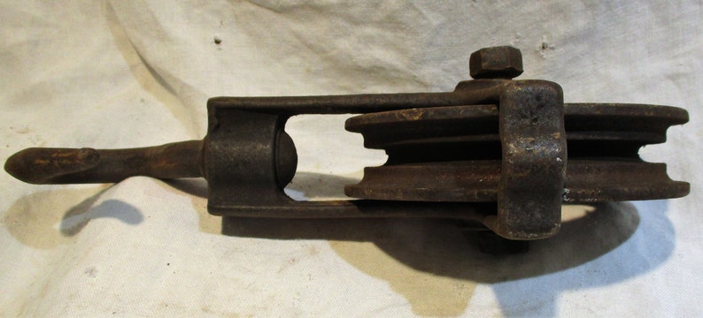 May include: A vintage cast iron pulley with three wheels. The pulley has a hook on one end and a metal loop on the other end.