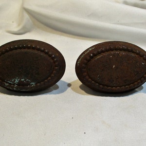 May include: Two oval-shaped, rusty metal drawer pulls with a beaded edge.