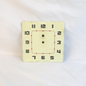 May include: A square, off-white clock face with black numerals and a dotted red and black border. The word "Telechron" is printed in the center. The clock face has a vintage aesthetic.