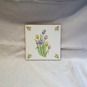 May include: A white ceramic tile with a floral design featuring a bouquet of pink, purple, and yellow tulips with green leaves and stems.