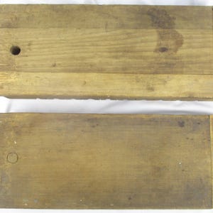 May include: Two rectangular wooden blocks with a natural light brown finish. Each block features a smooth surface with visible wood grain, a small circular hole on one end, and a distinct vertical seam near the opposite edge of the wood.