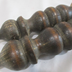 May include: Two dark brown wooden finials with a twisted design. The finials are made of wood and have a rough texture.