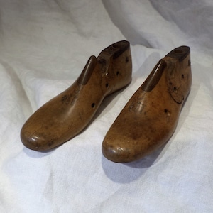 May include: A pair of antique wooden shoe lasts, used by shoemakers to shape and form shoes. The lasts are made of light brown wood and have a worn, rustic appearance.