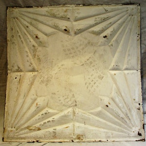 May include: A white ceiling tile with a geometric design. The tile has a raised pattern of overlapping triangles that create a starburst effect.