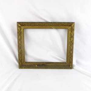 May include: A rectangular, antique-style picture frame with an ornate, embossed design. The frame is a muted gold color, with a slightly distressed finish. The frame is empty, with no picture or artwork inside.
