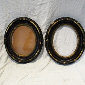 May include: Two oval-shaped picture frames with black wood and gold accents. The frames are empty.