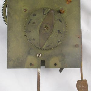 May include: A close-up of a vintage clock mechanism. The brass-colored plate features gears, a pendulum, and other components. The mechanism shows signs of age and wear, with some rust visible. The overall design is intricate and detailed.