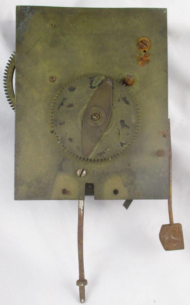 May include: A close-up of a vintage clock mechanism. The brass-colored plate features gears, a pendulum, and other components. The mechanism shows signs of age and wear, with some rust visible. The overall design is intricate and detailed.