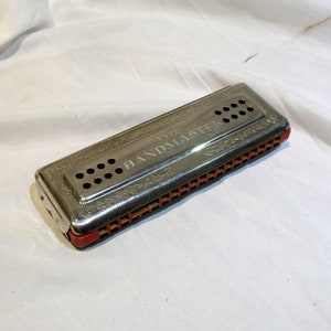 May include: A silver harmonica with red trim and the words "The Bandmaster" engraved on the top.
