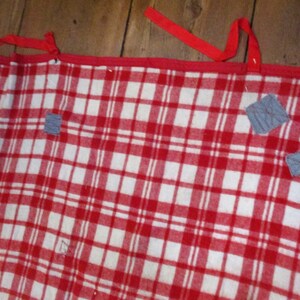 May include: Red and white checkered blanket with gray fabric patches sewn on. The blanket has red ties on the top edge.