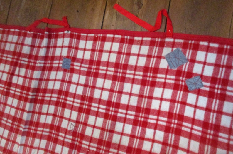 May include: Red and white checkered blanket with gray fabric patches sewn on. The blanket has red ties on the top edge.