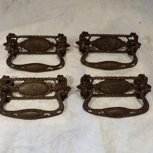 May include: Four antique brass drawer pulls with an ornate design. Each pull features a rope-like border, an oval center, and a decorative handle.