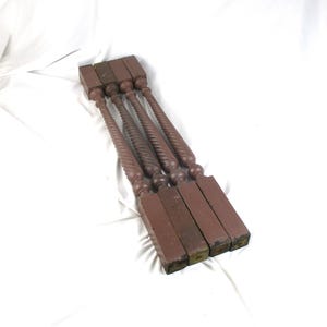 May include: Four antique, reddish-brown wooden balusters with a twisted spindle design. The balusters have a square base and a rounded top. They are arranged diagonally on a white surface.