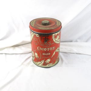 May include: A vintage red coffee tin with gold floral designs and the word "COFFEE" in elegant script. The tin has a lid with a small knob and the text "Hellick Coffee Co."