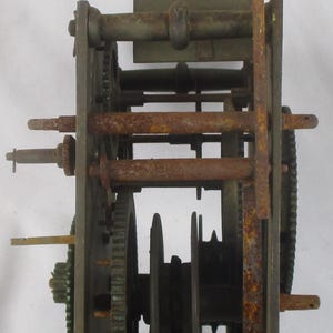 May include: An antique clock movement with visible gears, rods, and a pendulum mount. The metal components show signs of age and rust, suggesting a vintage piece. The mechanism is mounted on a rectangular frame.