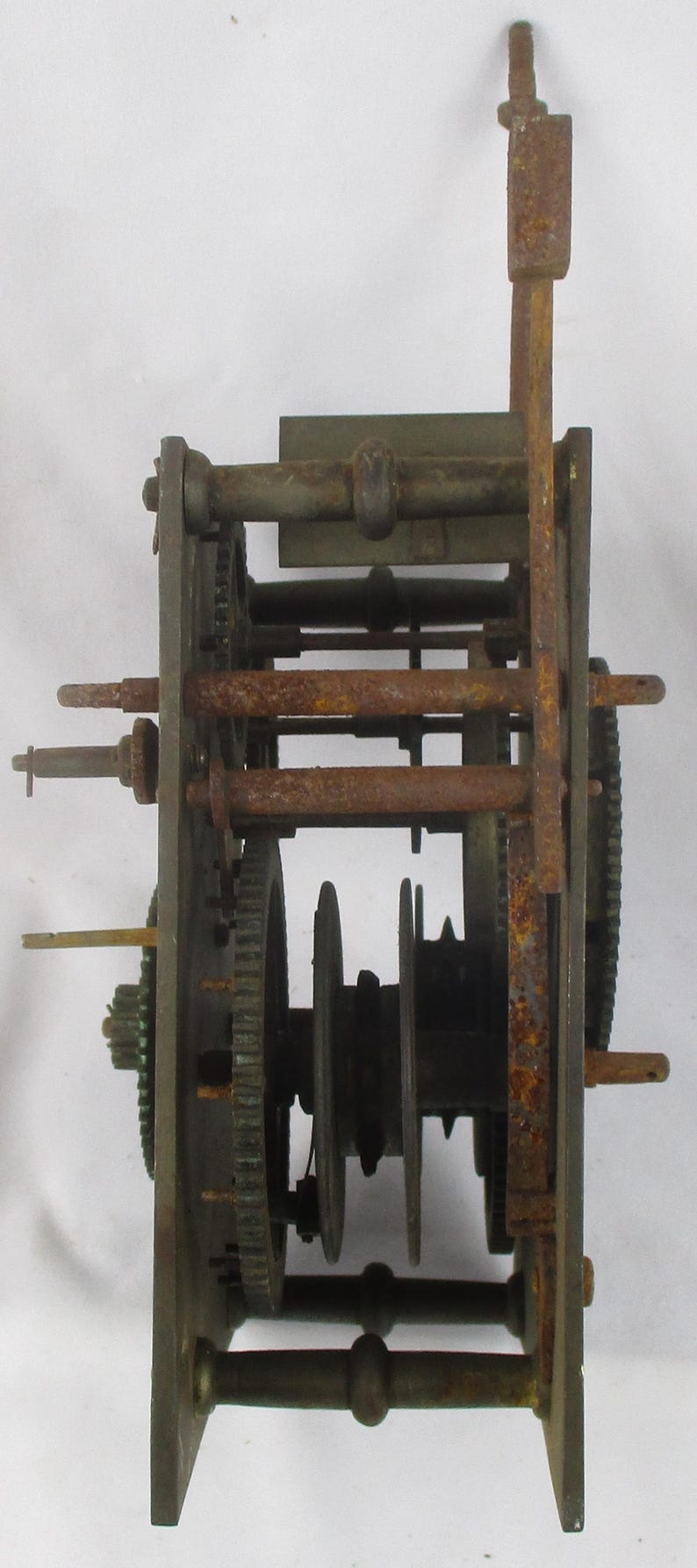 May include: An antique clock movement with visible gears, rods, and a pendulum mount. The metal components show signs of age and rust, suggesting a vintage piece. The mechanism is mounted on a rectangular frame.