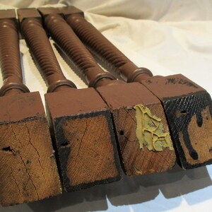 May include: Four turned wooden legs with square bases. The legs are dark brown and have a spiral design. The bases are showing signs of wear and tear.