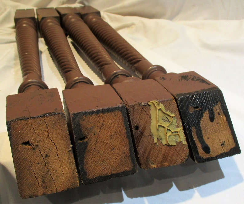 May include: Four turned wooden legs with square bases. The legs are dark brown and have a spiral design. The bases are showing signs of wear and tear.