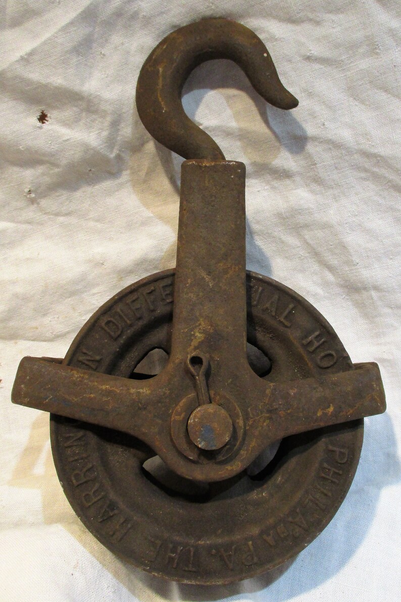 Pu&ograve; includere: Una carrucola in ghisa vintage con un gancio, etichettata "The Val. Ho. Differential Pulley Harlem, N.Y."