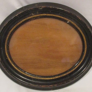 May include: An oval-shaped picture frame with a black wooden frame and a gold rope design around the edge.