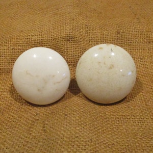 May include: Two white ceramic knobs with a textured surface. The knobs are round and have a slight off-white color.