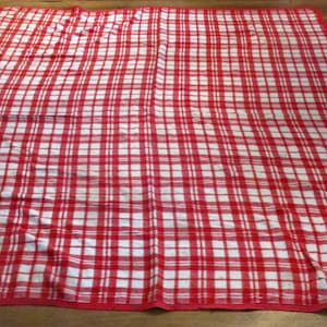 May include: A red and white checkered picnic blanket with a red border. The blanket is folded in half and has two ties on the side.