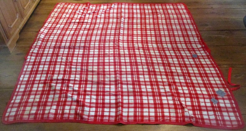 May include: A red and white checkered picnic blanket with a red border. The blanket is folded in half and has two ties on the side.