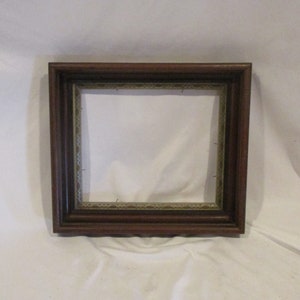 May include: A dark brown wooden picture frame with a gold-colored inner border. The frame has a simple, classic design.