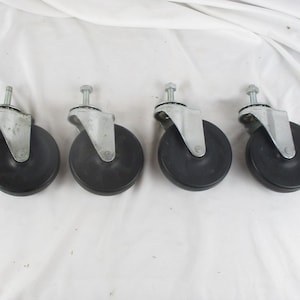 May include: A set of four swivel casters, each featuring a black circular wheel attached to a silver-toned metal mounting bracket with a threaded bolt stem extending from the top, designed for mobility on furniture or equipment bases.