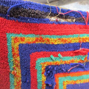 May include: A close-up of a colorful, hand-woven rug with a geometric pattern. The rug is made of different colored yarns, including red, blue, green, and yellow. The rug is frayed and worn in some areas, giving it a vintage look.
