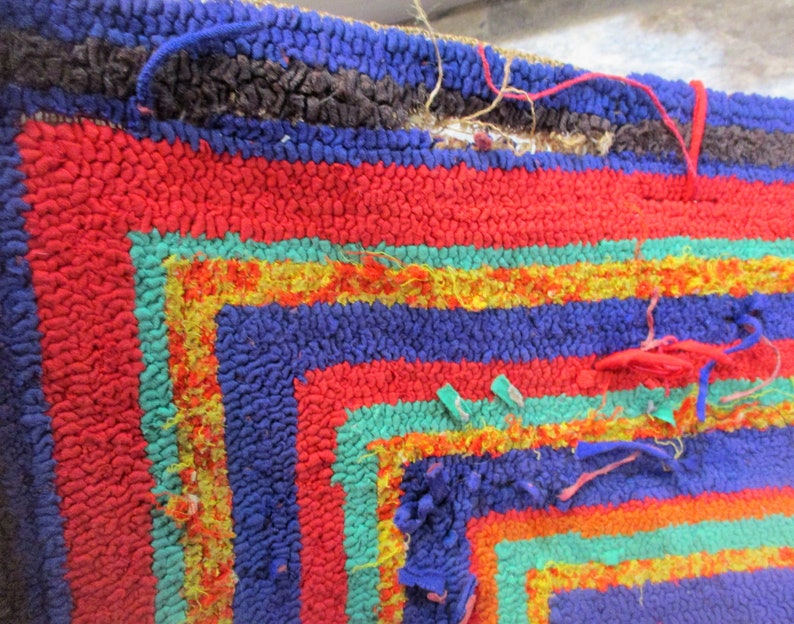 May include: A close-up of a colorful, hand-woven rug with a geometric pattern. The rug is made of different colored yarns, including red, blue, green, and yellow. The rug is frayed and worn in some areas, giving it a vintage look.