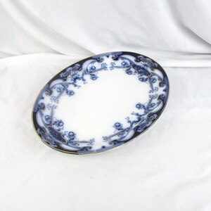 May include: Oval-shaped antique porcelain dish with a white center and a blue floral border. The rim is trimmed with gold. The dish is set against a white background.