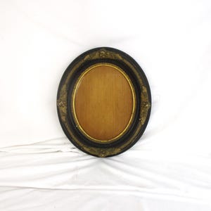 May include: Oval picture frame with a black wood exterior and gold accents. The frame has a decorative design with a raised edge and a gold inner border.