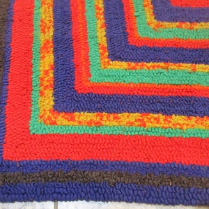 May include: Close-up of a colorful braided rug with a geometric pattern. The rug has stripes of red, blue, green, and yellow.