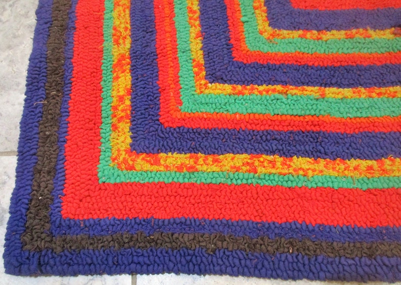 May include: Close-up of a colorful braided rug with a geometric pattern. The rug has stripes of red, blue, green, and yellow.