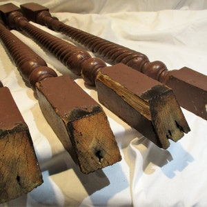 May include: Four turned wooden balusters with square bases. The balusters are brown and have a spiral design. The bases are showing signs of wear and tear.