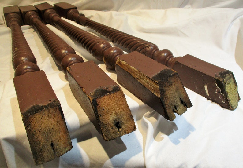 May include: Four turned wooden balusters with square bases. The balusters are brown and have a spiral design. The bases are showing signs of wear and tear.