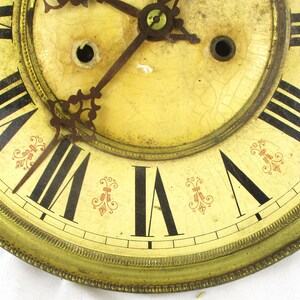Peut inclure: Cadran d'horloge ancien avec des chiffres romains noirs sur un fond cr&egrave;me. Le cadran de l'horloge pr&eacute;sente des accents floraux rouges d&eacute;coratifs et un cadre en m&eacute;tal dor&eacute;. Les aiguilles de l'horloge sont visibles et le cadran montre des signes d'&acirc;ge.
