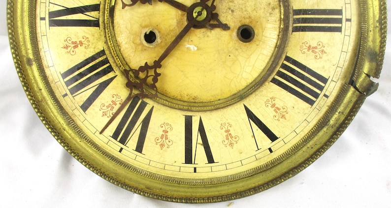 Peut inclure: Cadran d'horloge ancien avec des chiffres romains noirs sur un fond cr&egrave;me. Le cadran de l'horloge pr&eacute;sente des accents floraux rouges d&eacute;coratifs et un cadre en m&eacute;tal dor&eacute;. Les aiguilles de l'horloge sont visibles et le cadran montre des signes d'&acirc;ge.