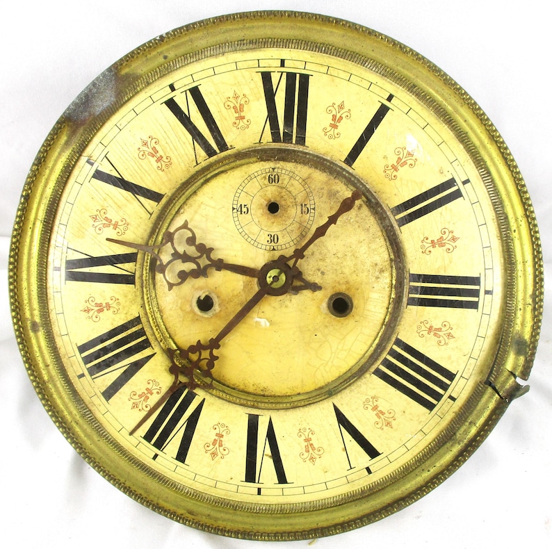 Peut inclure: Cadran d'horloge ancien avec un fond cr&egrave;me et des chiffres romains noirs. Le cadran a un cadre en m&eacute;tal dor&eacute; et des accents floraux rouges d&eacute;coratifs. Les aiguilles sont marron fonc&eacute;, et un petit cadran indique les secondes.