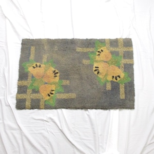 May include: Rectangular rug with a gray background and a floral design. The rug features yellow flowers with black details and green leaves, set against a grid pattern. The rug is placed on a white surface.