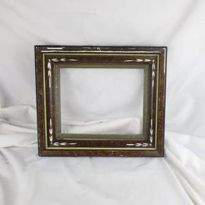 May include: A rectangular picture frame with a dark brown wood grain finish. The frame has a green interior and a thin gold-colored accent line. White arrow-shaped details are painted along the outer edge. The frame is empty.