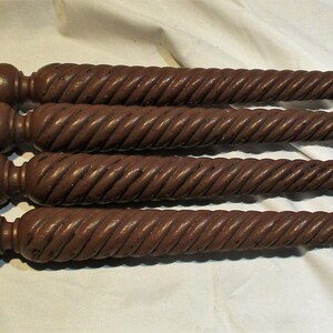 May include: Four dark brown wooden table legs with a twisted design. Each leg has a rounded top and a square base.